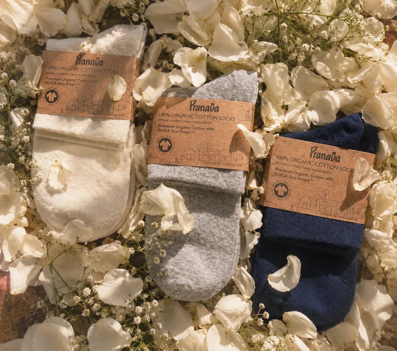 Three pairs of Pranava socks in their card wraps, resting on white flowers