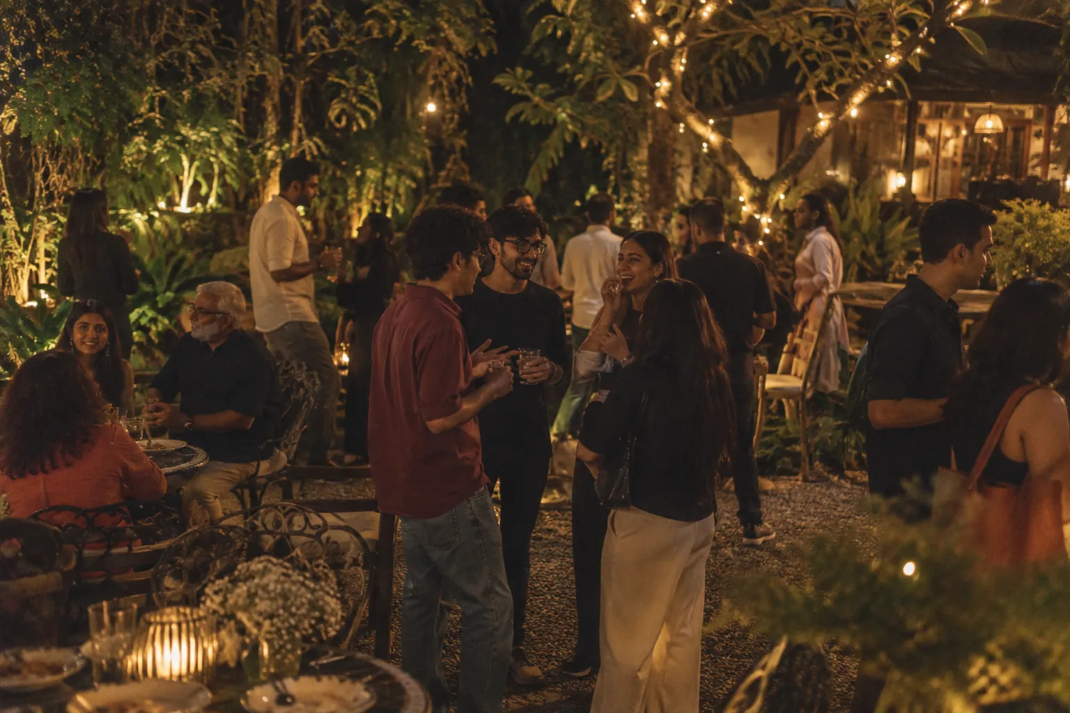 Members standing and talking in a garden lit with fairy lights
