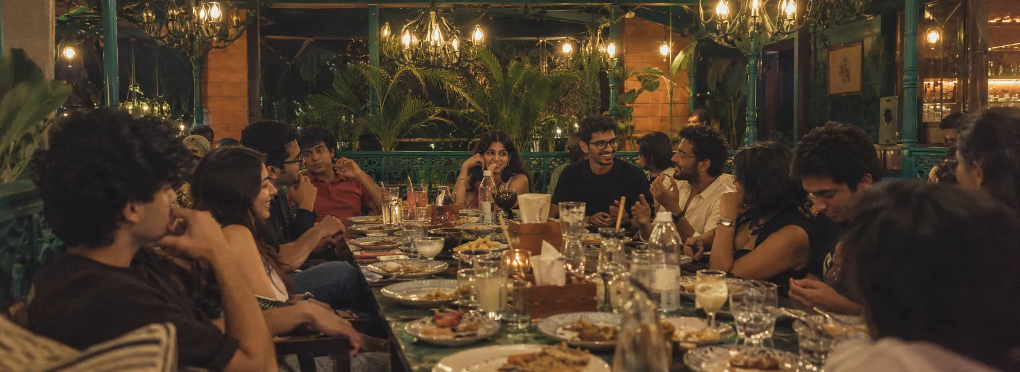 A long table of Roots members under string lights, mid-conversation